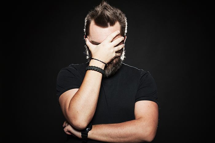 A bearded man holding his hand to his face on a black background