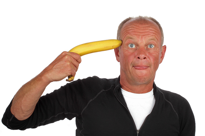 A stressed out man holding a banana to his head