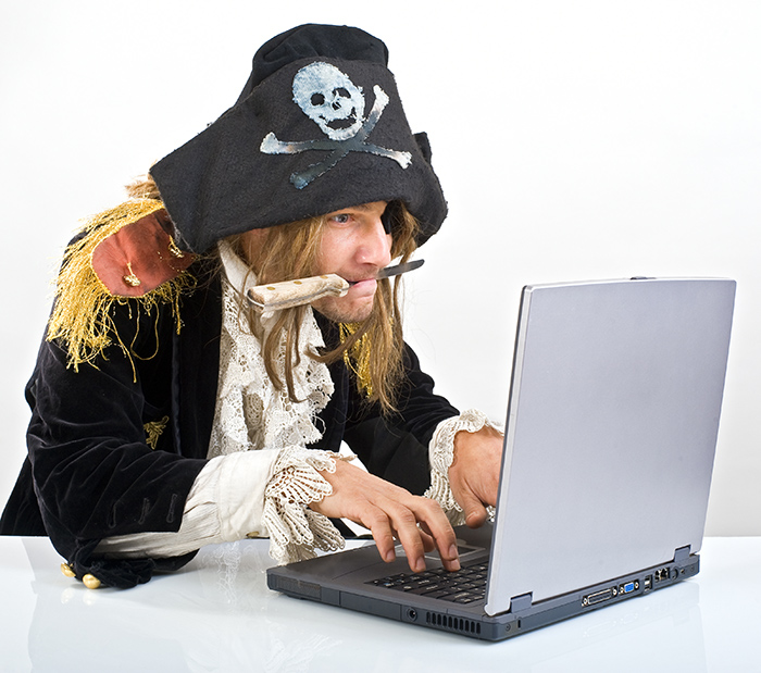 A pirate with a knife in his mouth sitting in front of a laptop